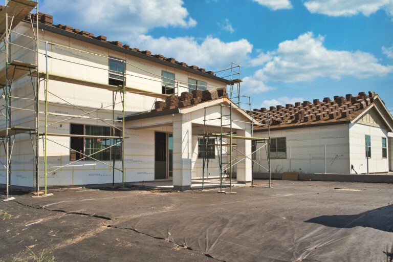 Concrete roofing tile installation with roof tiles lined up in rows on a residential modern home build with a patio cover and scaffolds and backyard preparation